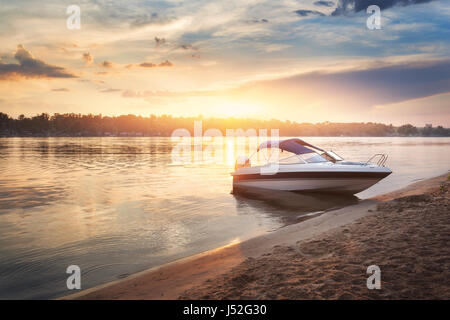 Colorful sunset with boat ot the river bank. Summer landscape with pleasure boat, river, bright sky with clouds and yellow sunlight reflected in water Stock Photo