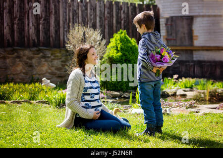 Young pregnant woman, receiving bouquet of colorful flowers from her child for Mothers Day, sitting in a beautiful spring blooming garden. Mother's da Stock Photo