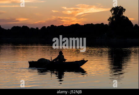 Silhouette of traditional egyptian bedouin fisherman in rowing boat on river Nile at dusk sunset Stock Photo