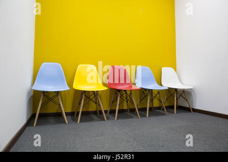 Five multi-colored chairs with yellow wall in office. Stock Photo