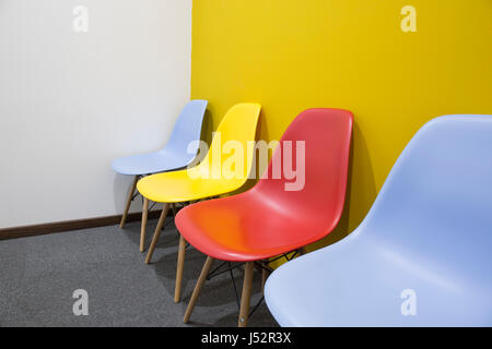 Five multi-colored chairs with yellow wall in office. Stock Photo