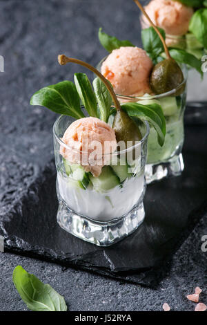 Verrines appetizer with salmon pate, red caviar, cucumber, cream cheese, herbs, capers in glasses served with pink salt and basil on black slate stone Stock Photo