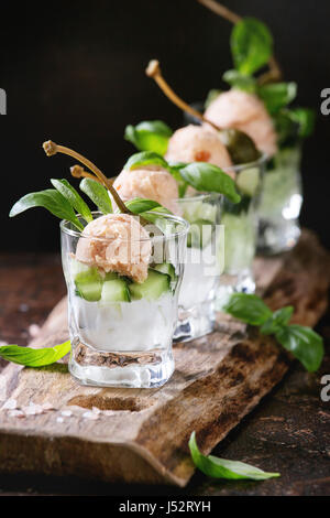 Verrines appetizer with salmon pate, red caviar, cucumber, cream cheese, herbs, capers in glasses served with pink salt and basil on wooden serving bo Stock Photo