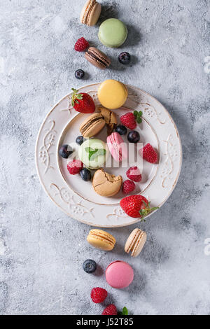 Variety of colorful french sweet dessert macarons with different fillings served on white vintage plate with spring flowers and berries over gray text Stock Photo