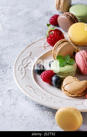 Variety of colorful french sweet dessert macarons with different fillings served on white vintage plate with spring flowers and berries over gray text Stock Photo