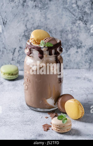 Chocolate coffee milkshake with ice cream scoop served in glass mason jar with a variety of macarons biscuit on gray texture background. Summer sweet Stock Photo