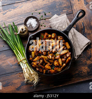 Fried potatoes roasted with porcini mushrooms in cooking pan on wooden background Stock Photo