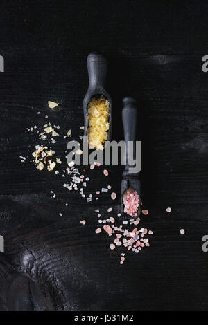 Variety of colorful salt yellow saffron and pink himalayan in wooden spoons over black burnt wood background. Top view with space Stock Photo