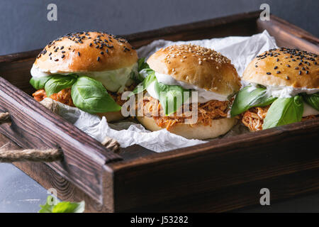 Homemade mini burgers with pulled chicken, basil, mozzarella cheese and yogurt sauce on wooden tray with baking paper over gray texture background. He Stock Photo