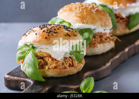 Homemade mini burgers with pulled chicken, basil, mozzarella cheese and yogurt sauce on wooden serving board over gray texture background. Close up. H Stock Photo