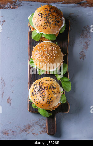 Homemade mini burgers with pulled chicken, basil, mozzarella cheese and yogurt sauce on wooden serving board over gray texture background. Top view wi Stock Photo