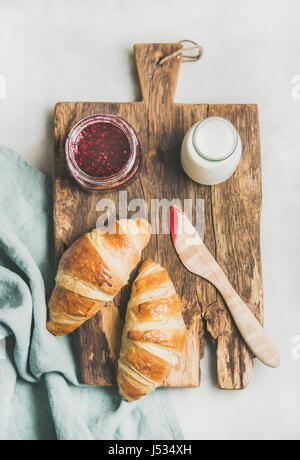 Breakfast concept. Freshly baked croissants with raspberry jam and milk in bottle on rustic wooden board over light grey marble background, top view Stock Photo