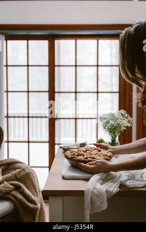 A woman is photographed as she is placing a freshly baked apple pie on the table. Stock Photo