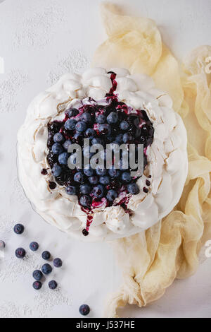 Homemade meringue cake Pavlova with whipped cream, fresh blueberries and blueberry sauce on vintage cake stand on white concrete texture background, g Stock Photo