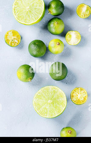 Whole, sliced lime and mini limes over gray stone texture background. Top view, space Stock Photo