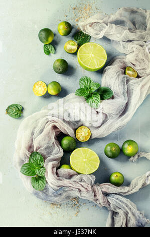 Ingredients for mojito cocktail, whole, sliced lime and mini limes, mint leaves, brown crystal sugar over gray stone texture background with gauze tex Stock Photo