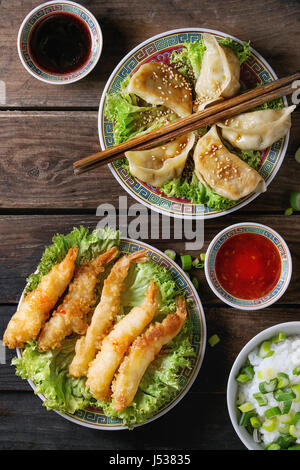 Fried tempura shrimps and gyozas potstickers on lettuce salad with sauces and rice. Served in traditional china plate with chopsticks over old wooden  Stock Photo