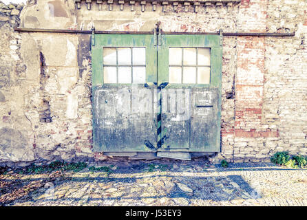 Large old warehouse door with peeling green paint on brick wall. Stock Photo