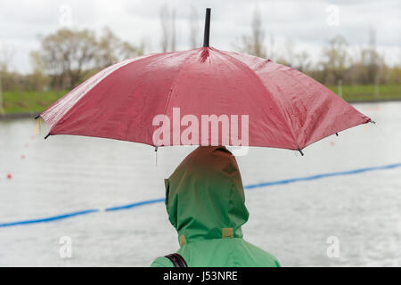 Someone wearing a green raincoat and holding a red umbrella on a rainy day Stock Photo