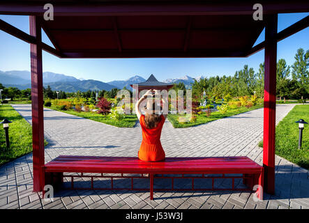 Woman in orange dress with hand in heart shape sitting on the bench in the Japanese Pagoda garden Stock Photo