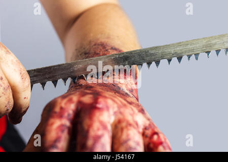 cutting into bloody hand with saw blade in front of grey background Stock Photo