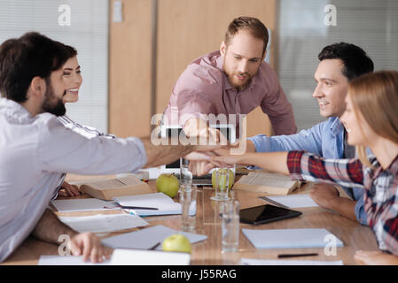 Group of positive workers holding hands together over workplace Stock Photo
