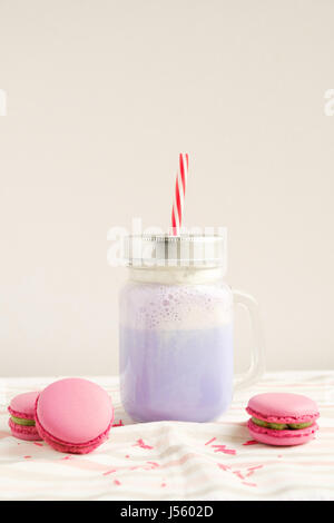 Purple coffee in stylized mason jar cup with macarons and colorful decoration. Blueberry milk shake, cocktaill, frappuccino. Unicorn coffee. Unicorn f Stock Photo