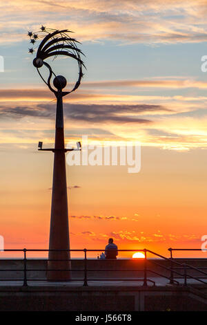 Southport, Merseyside. 16th May 2017. UK Weather.  After a day of heavy rain showers & gusty winds, a man sits on the sea wall to watch a stunning sunset as it rests over Southport Pier in Merseyside.  Credit: Cernan Elias/Alamy Live News Stock Photo