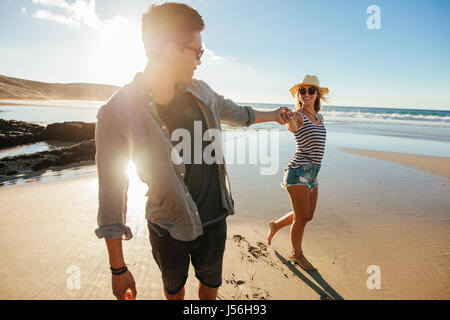 Shot of loving young couple holding hands and walking on seashore. Young man and woman walking on beach on a summer day. Stock Photo