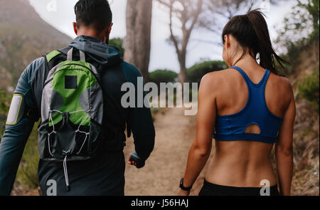 Rear view shot of fit young couple walking on mountain trail. Young man and woman walking through country path in morning. Stock Photo