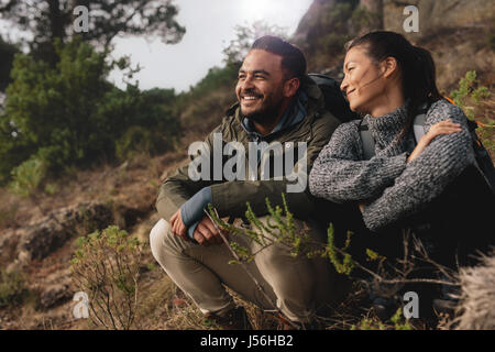 Young couple out on hike in mountains. Relaxed young man and woman sitting on country path. Stock Photo