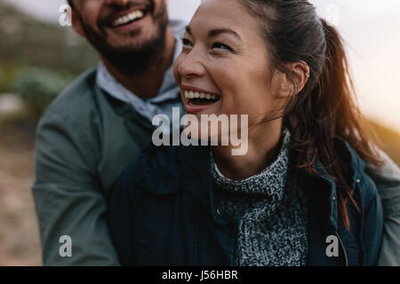 Smiling asian woman being embraced by her boyfriend from behind. Couple enjoying on vacation. Stock Photo
