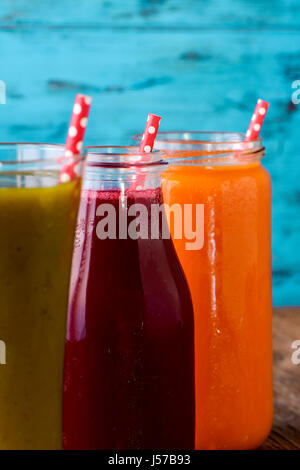 closeup of three different fresh smoothies served in a glass, a glass jar and a glass bottle with red drinking straws patterned with white dots, on a  Stock Photo