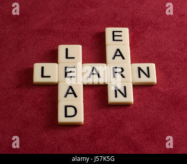 Crossword puzzle with words Learn, Lead and Earn. Leadership concept. Ivory tiles with capital letters on red velure. Stock Photo