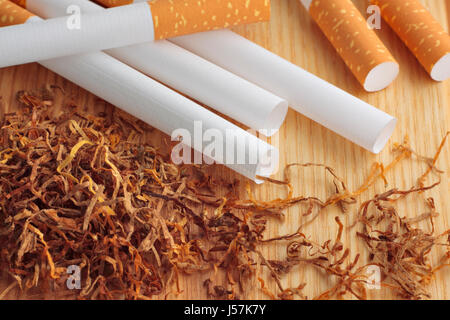 Empty cigarette tubes and tobacco on wooden board. Close up view. Stock Photo
