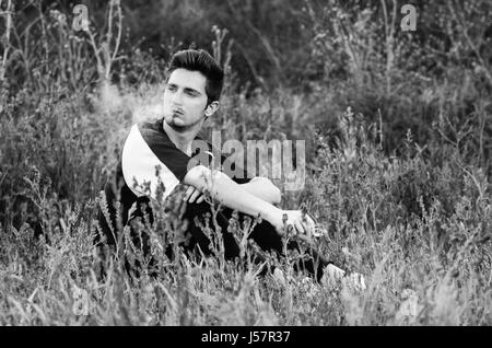 black and white portrait of lonely man smokong a cigarette in a field Stock Photo