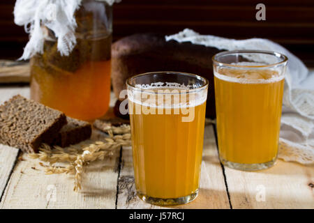 Traditional Russian cold rye drink Kvas in a glass and a jug on a wooden table. Kvass from bread, rye malt, sugar and water. Stock Photo