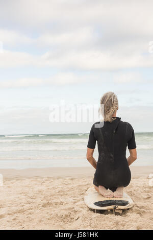 Rear view of woman kneeling on surfboard against sea Stock Photo