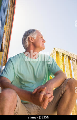 Senior man looking away while sitting at hut against clear sky Stock Photo