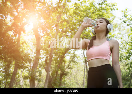 young beautiful asian fitness athlete woman drinking water after work out exercising at summer green park. Concept of healthy lifestyle Stock Photo