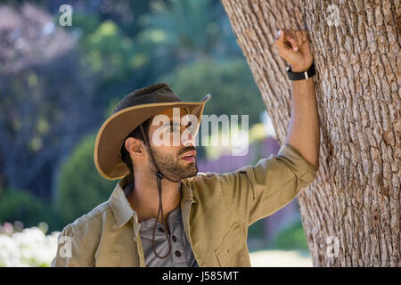 Thoughtful man leaning on tree trunk in forest Stock Photo