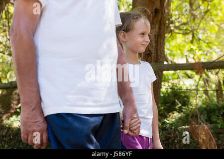 Grandfather and granddaughter holding hands while walking in the forest Stock Photo