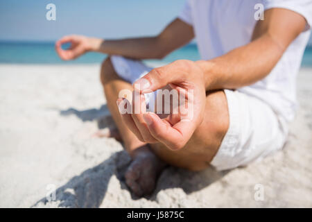 Low section of man practicing meditation at beach on sunny day Stock Photo