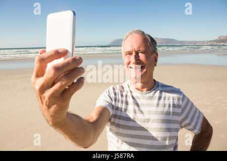 Happy senior man taking selfie through mobile phone at beach on sunny day Stock Photo