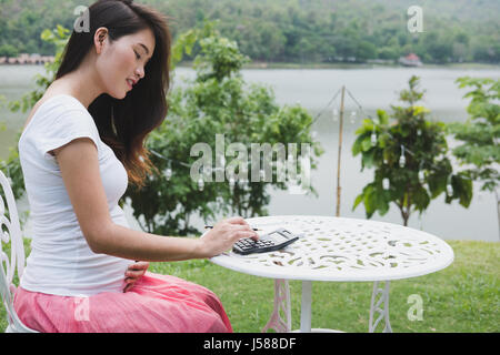 young asian pregnant woman plans the family budget with calculator. beautiful female calculating her domestic bills in garden Stock Photo