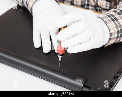 service engineer in white gloves disassembles laptop with screwdriver Stock Photo