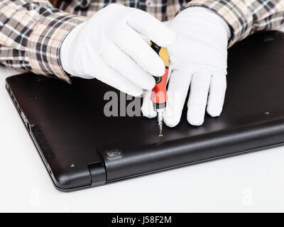 serviceman in white gloves disassembles laptop with screwdriver Stock Photo