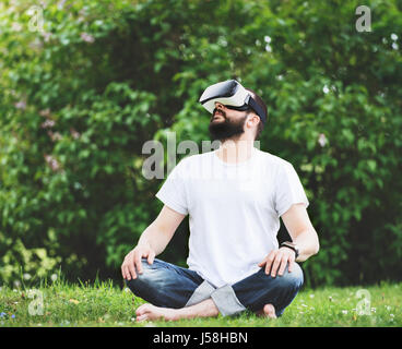 Young bearded man wearing virtual reality goggles sitting in his garden. Lifestyle VR fun and relax concept. Stock Photo