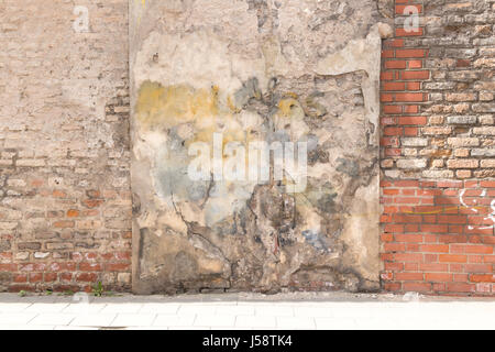 Old weathered vintage brick wall with broken plaster and pavement on the ground. Grungy urban background. Stock Photo