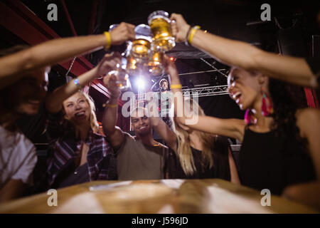 Happy friends toasting beer glasses while sitting at table in club Stock Photo